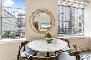 Una habitación con una mesa redonda, sillas, un espejo y una ventana con vista a la ciudad.