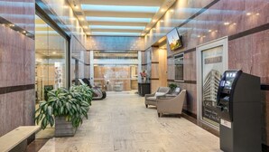 Un vestíbulo de hotel con mostrador de recepción, zona de estar, cajero automático y plantas en macetas.