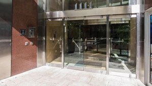Una entrada de edificio moderna con puertas de vidrio, estructura metálica y pared de ladrillo rojo.