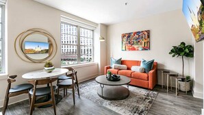 Una sala de estar moderna con una mesa redonda, un sofá naranja y un ventanal con vistas a la ciudad.