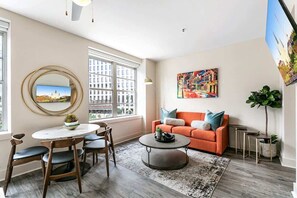 Una sala de estar moderna con una mesa redonda, un sofá naranja y un ventanal con vistas a la ciudad.