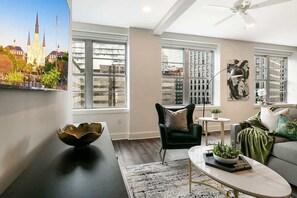 A modern living room with a large window, a black table, a green armchair, a white coffee table, and a small side table with a plant. - Premier Four Bedroom Residence-Sleeps 12 (New Orleans)