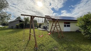 A backyard with a swing set, a ladder, and a house with solar panels. - 4-person vacation home with a private boat dock, right on the lake, with a canoe and sauna in Otterndorf (Otterndorf)