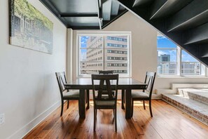 Un comedor con una mesa y sillas, un ventanal con vistas a la ciudad y una escalera que sube a un nivel superior.