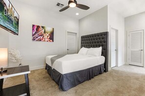 Quarto com cama, ventilador de teto, escrivaninha com luminária e televisão na parede.