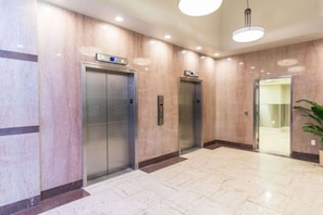 Área de elevador moderna com paredes de mármore e chão ladrilhado.