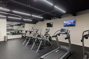 Ein Fitnessraum mit Laufbändern, Crosstrainern und einem Fernsehbildschirm.