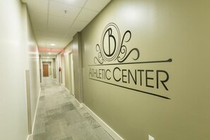 Ein Flur mit einem Wandzeichen, das 'ATHLETIC CENTER' zeigt, und einer Tür am Ende.