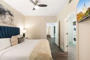 Ein Hotelzimmer mit Bett, Deckenventilator, Wand-Fernseher und Blick auf ein Gebäude durch eine offene Tür.
