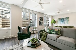 Una sala de estar moderna con sofá, sillón y mesa de centro, ventanas amplias y ventiladores de techo.