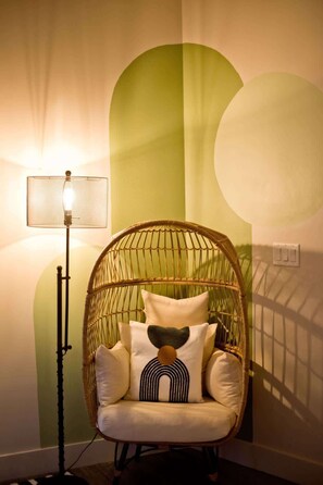 Una silla de mimbre con cojines y una lámpara de pie en una habitación con paredes verdes y un interruptor de luz.
