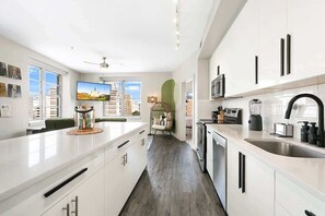 A modern kitchen with white cabinetry, a large island, and a view of the cityscape through the windows. - Two Bedroom Residence-Sleeps 5 (New Orleans)