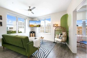 Una sala de estar moderna con un sofá verde, una televisión, un sillón de ratán y una alfombra estampada.