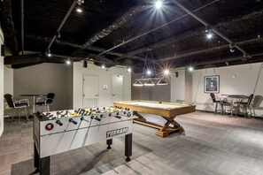 Une pièce équipée d’un baby-foot, d’une table de billard et d’un espace détente avec des sièges.