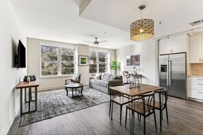 Une cuisine moderne équipée d’un grand réfrigérateur, d’une table à manger et de chaises. Le salon comprend un canapé et une table basse, ainsi qu’un ventilateur de plafond.