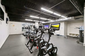 Une salle de sport équipée de vélos d’appartement, de tapis de course et d’un écran de télévision.