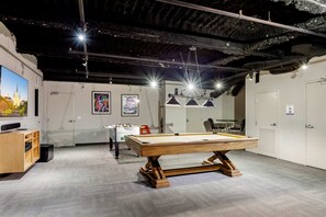 Une table de billard se trouve dans une pièce dotée d’un plafond haut, de murs blancs et d’une grande fenêtre.