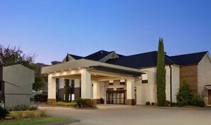 Ein modernes Hotel mit überdachter Eingangsparte, großen Fenstern und einem gepflegten Rasen.