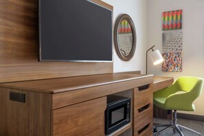 Ein moderner Arbeitsraum mit einem Holztisch, einer schwarzen Mikrowelle, einem grünen Stuhl, einem Flachbildfernseher und abstrakter Wandgestaltung.