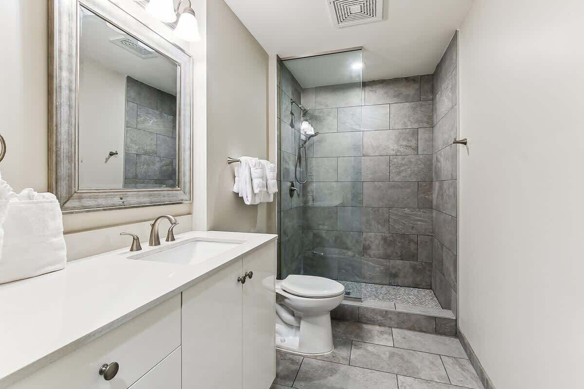 A bathroom with a white sink, a toilet, a shower with glass doors, and a large mirror.