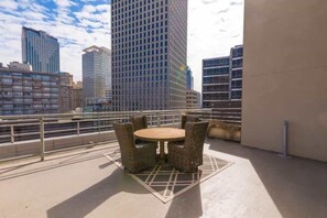 Un balcón con mobiliario de mimbre, vistas a edificios de la ciudad y una barandilla de metal.