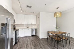 Une cuisine moderne avec des meubles blancs, des appareils en acier inoxydable et un coin repas comprenant une table en bois et des chaises en métal.