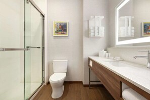 Ein modernes Badezimmer mit Duschkabine aus Glas, einer weißen Toilette, einem hölzernen Waschtisch mit Spiegel und zwei gerahmten Bildern an der Wand.