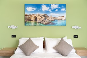 Camera d'albergo con un letto, pareti verdi, un quadro di un paesaggio costiero e due decorazioni a forma di pesce.