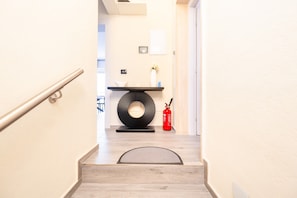 Una scala conduce a una stanza dal design moderno, con un decoro nero circolare al muro, un vaso bianco con fiori e un estintore rosso.