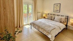 Un dormitorio con cama, mesita de noche, lámpara colgante, ventana con cortinas e imagen enmarcada en la pared.