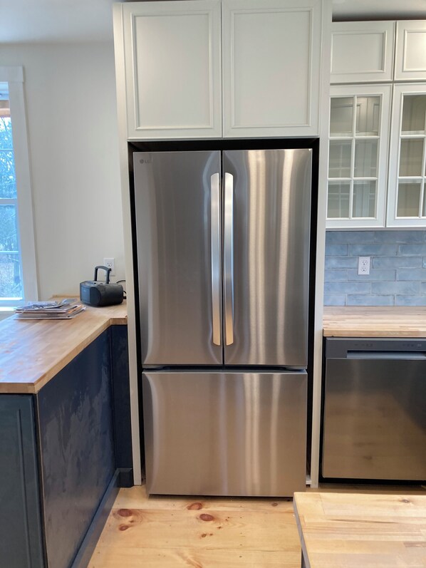 A stainless steel double-door refrigerator with a wooden countertop and cabinets.