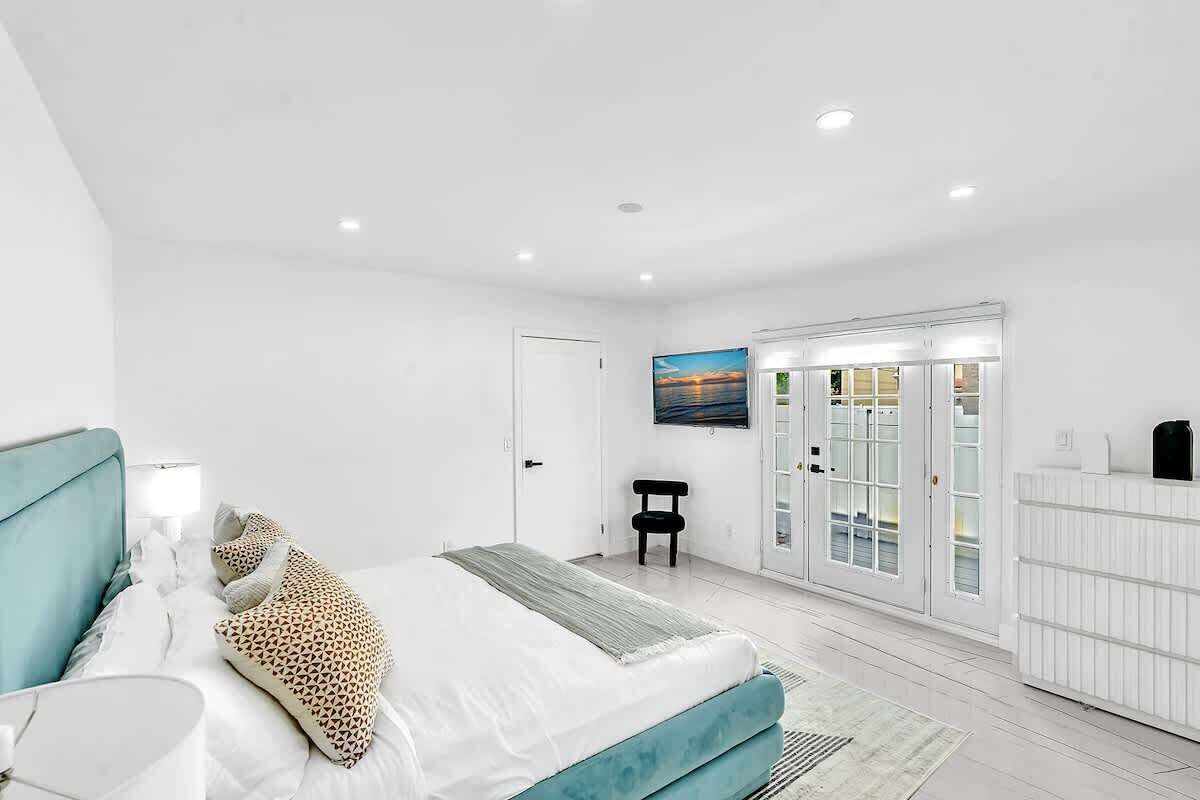 A modern bedroom with a bed, a chair, a wardrobe, and a door leading to a balcony.