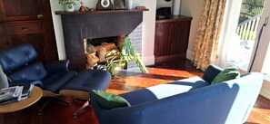 Un salon avec une cheminée, des meubles bleus, une table basse et une vue sur l’extérieur.