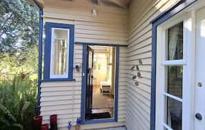 A house with a covered porch, a door leading to an interior room, and a small outdoor seating area with a bench and a rug.