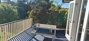A wooden deck with a table and chairs, surrounded by greenery and a white fence.