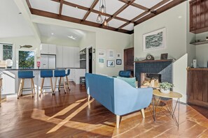 A modern kitchen with white cabinets, a dining area with blue chairs, and a fireplace.