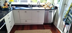 A kitchen with white cabinets, a stainless steel dishwasher, a black countertop, and a wooden floor.