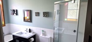 A bathroom with a white sink, mirror, toilet, and glass shower door.