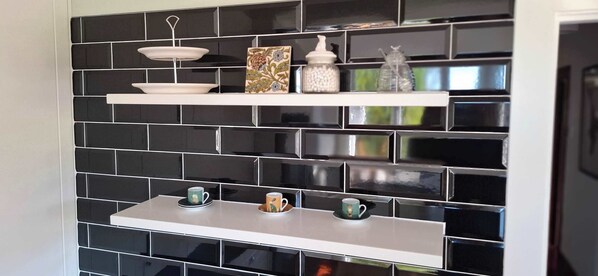 A kitchen with black tiled backsplash, white shelves, and decorative items.