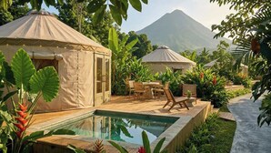 Un espace piscine agrémenté de deux yourtes, entouré de plantes tropicales et avec une montagne en toile de fond.