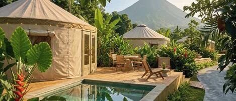A pool area with two yurts, surrounded by tropical plants and a mountain in the background.