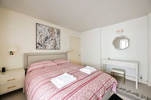 Ein Schlafzimmer mit Bett, Nachttischen, einem Schreibtisch, einem Spiegel und einem Bild an der Wand.