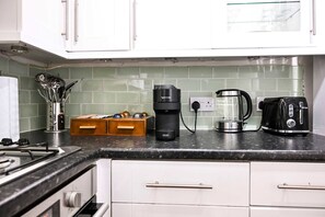 Eine Küche mit weißen Schränken, einer schwarzen Arbeitsplatte, einer Kaffeemaschine, einem Toaster und einem Wasserkocher.