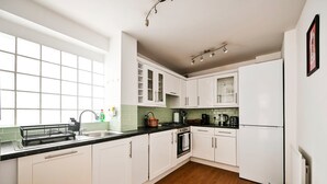 A modern kitchen with white cabinets, a black countertop, and a wooden floor. - Chelsea Modern - Stylish Hideaway (London)