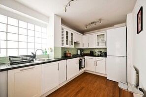 A modern kitchen with white cabinets, a black countertop, and a wooden floor. - Chelsea Modern - Stylish Hideaway (London)