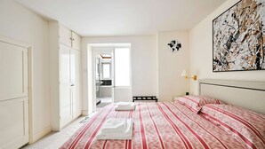 A bedroom with a bed, a wardrobe, a painting, and a view into another room. - Chelsea Modern - Stylish Hideaway (London)