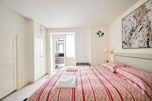 A bedroom with a bed, a wardrobe, a painting, and a view into another room. - Chelsea Modern - Stylish Hideaway (London)