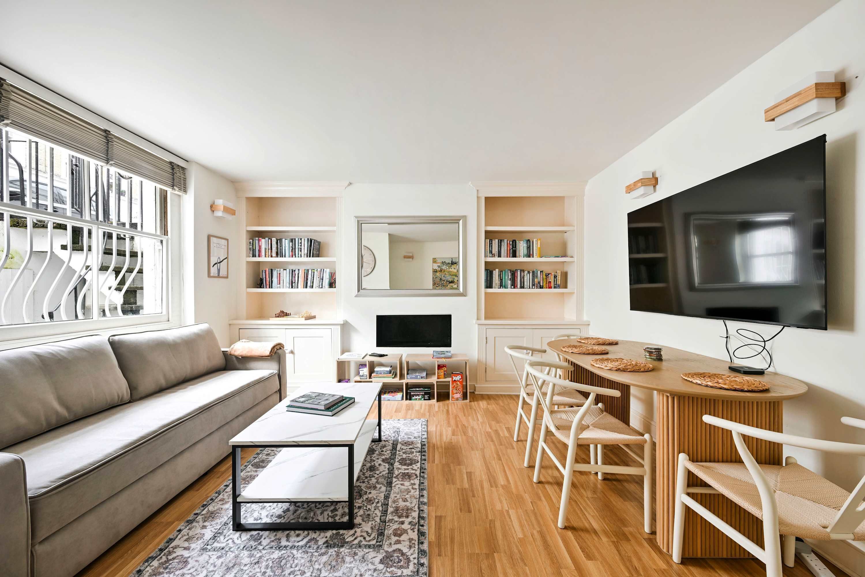 A modern living room with a sofa, coffee table, TV, bookshelves, and a dining area.
