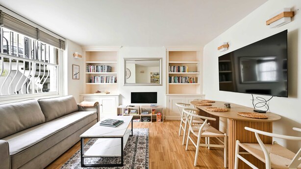 A modern living room with a sofa, coffee table, TV, bookshelves, and a dining area. - Chelsea Modern - Stylish Hideaway (London)