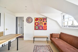 Ein modernes Wohnzimmer mit Holztisch, einer Bank, einer Couch, einem farbenfrohen abstrakten Gemälde und einer Uhr an der Wand.